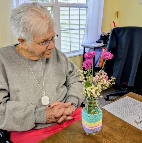 elderly woman admires a small vase she decorated full of flowers that she arranged.