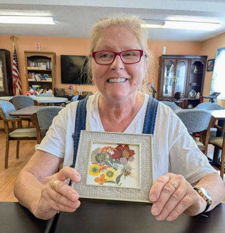 smiling woman holding up her framed pressed flower art